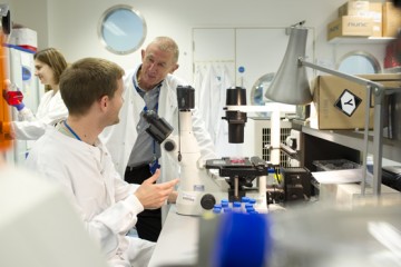 Professor Ian MacKenzie with a colleague who is using a microscope in a laboratory