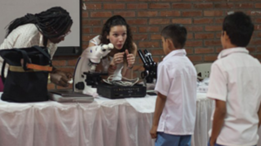 Dr María Duque-Correa in conversation with two young students who are approaching the table 