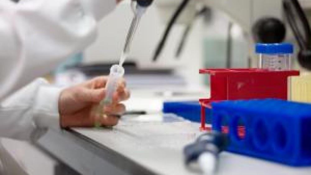 A laboratory technician with a sample tube injecting fluid into it