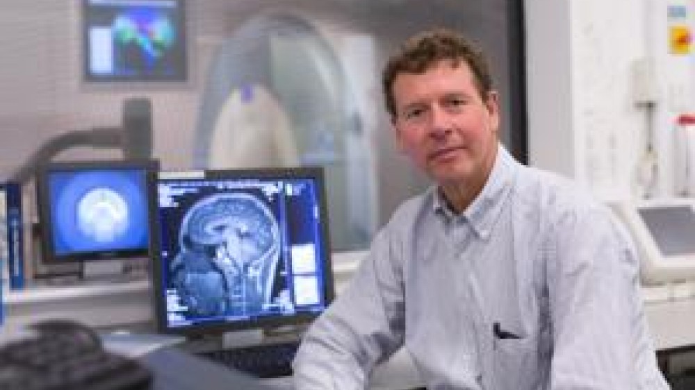 Professor Paul Matthews sitting by a desk with a monitor in the background