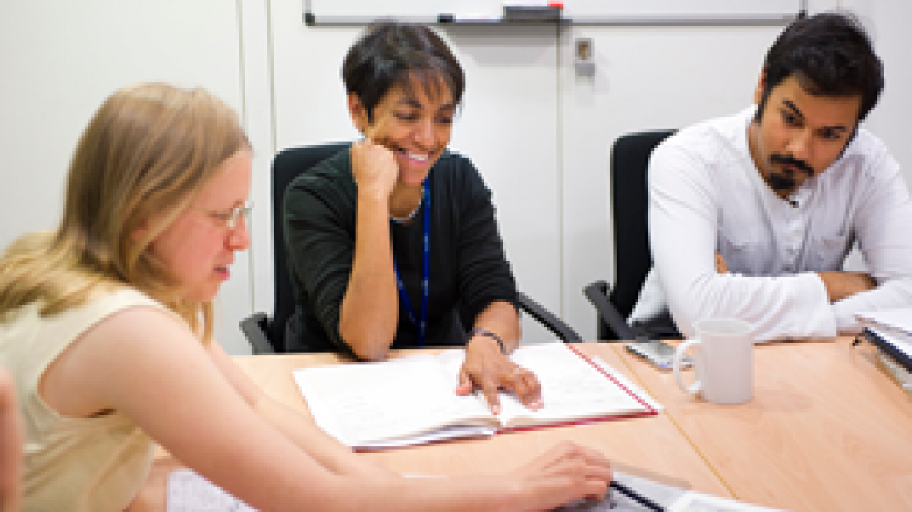 Three scientists sitting at a table discussing an open document