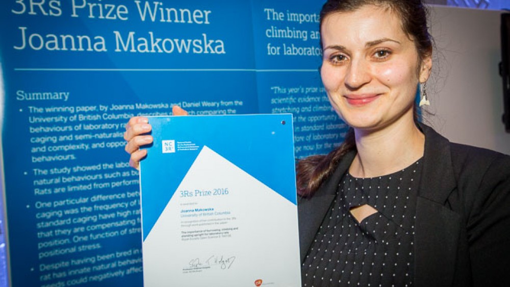 2016 Prize winner: Dr Joanna Makowska. Joanna is seen in front of a poster describing her work. She is holding up her prize certificate.