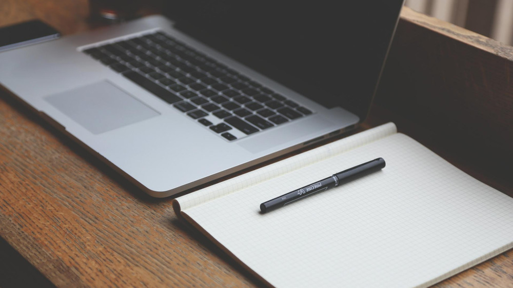 A laptop and blank sheet of paper with a pen are on a desk