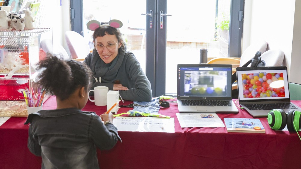 A scientist talking to a child at a public engagement event with resources on refining rodent housing.