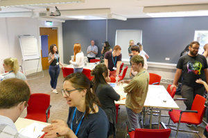 Students standing in a classroom in various discussion groups 