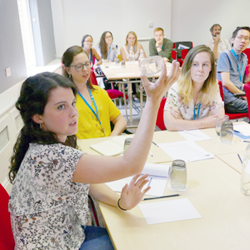 Students sitting in a classroom with the camera focused on a student demonstrating with her hand