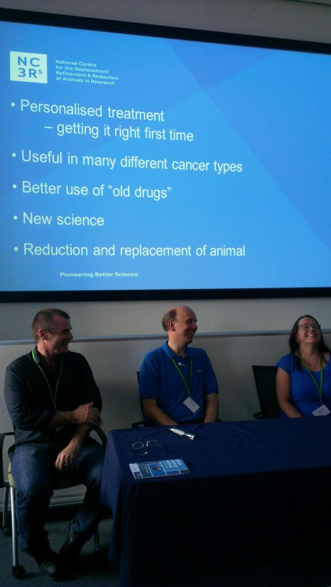 Professor John Greenman sitting down with two colleagues below a large screen