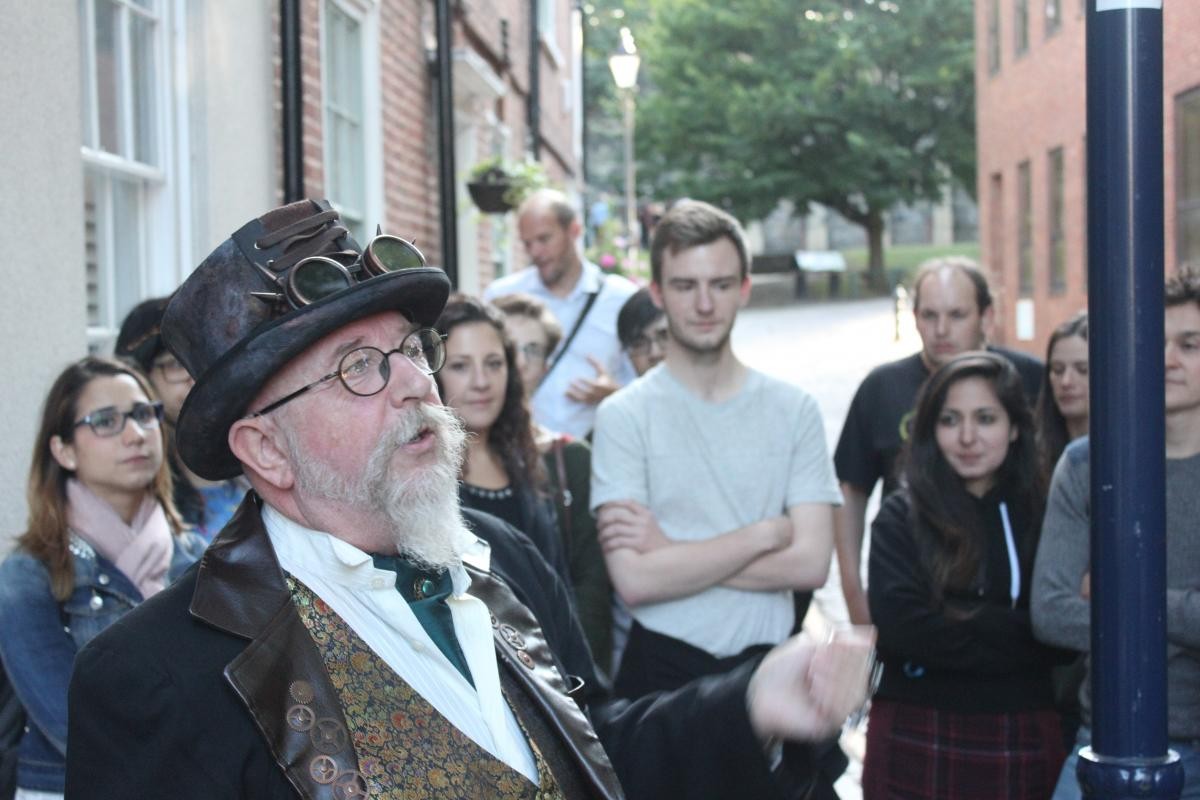 A man in a top hat is giving a speech with an audience in the background