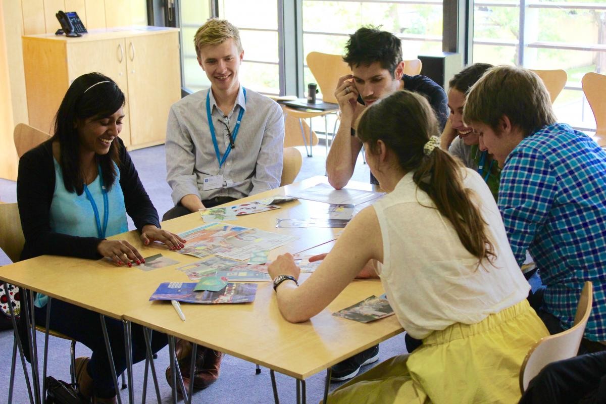 Students sitting around a table partaking in a public engagement exercises. The students were challenged to present their research using only pictures from magazines, and then using food