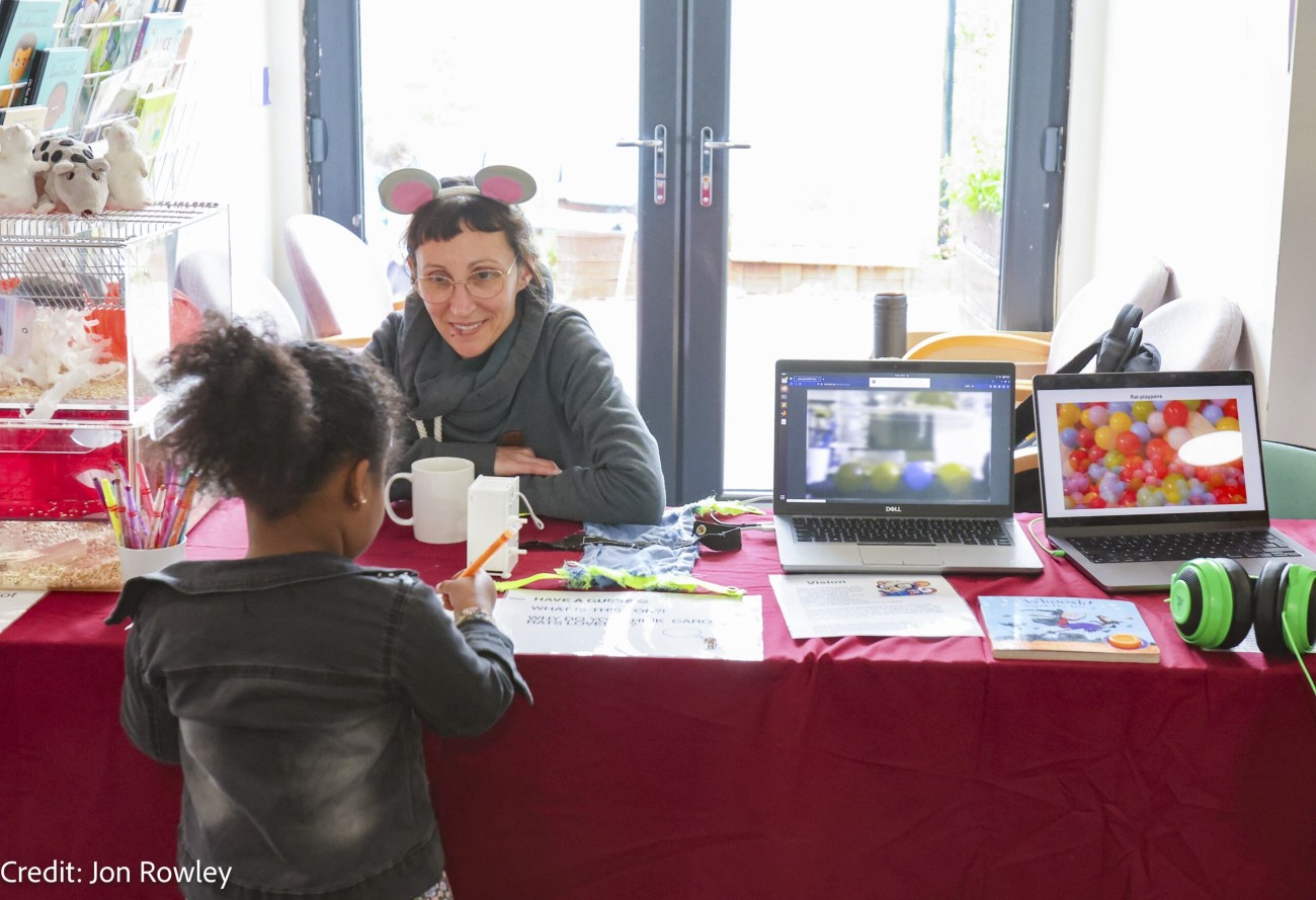 A scientist talking to a child at a public engagement event with resources on refining rodent housing.