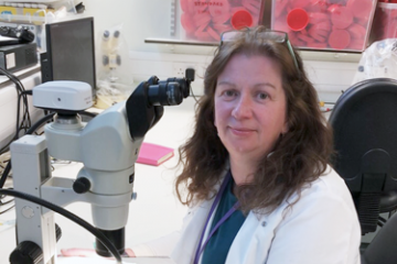 Professor Joanne Cable sitting down beside a microscope