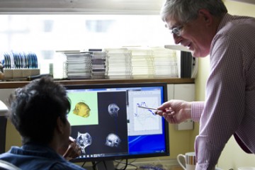 Professor Roger Lemon standing up while pointing to a screen monitor. A colleague is sitting down beside him