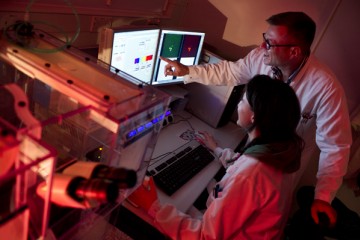 Two researchers looking at a screen. One is sitting and the other is standing pointing to the screen 