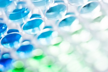 A stock image of round glass dishes containing blue and green liquid arranged closely together.