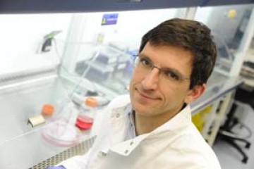 Dr Ludovic Vallier, winner of the 3Rs prize in 2011 can be seen sitting in a laboratory. He is wearing a white lab coat and purple gloves.